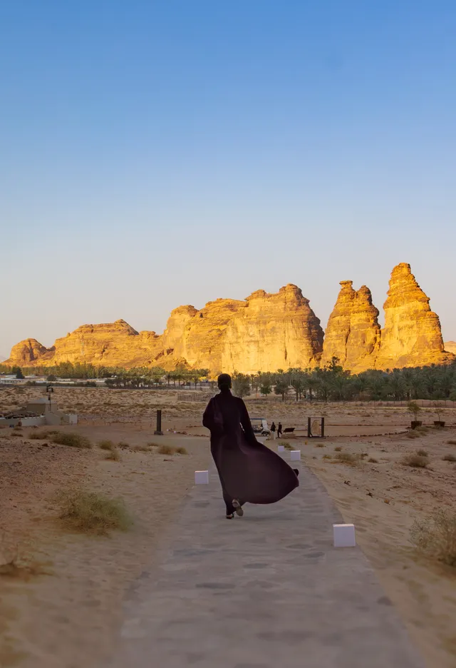 A visitor walking a path towards the AlUla oasis at sunrise