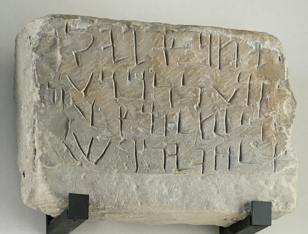 A limestone block on a museum mount, inscribed with four lines of Imperial Aramaic letters.