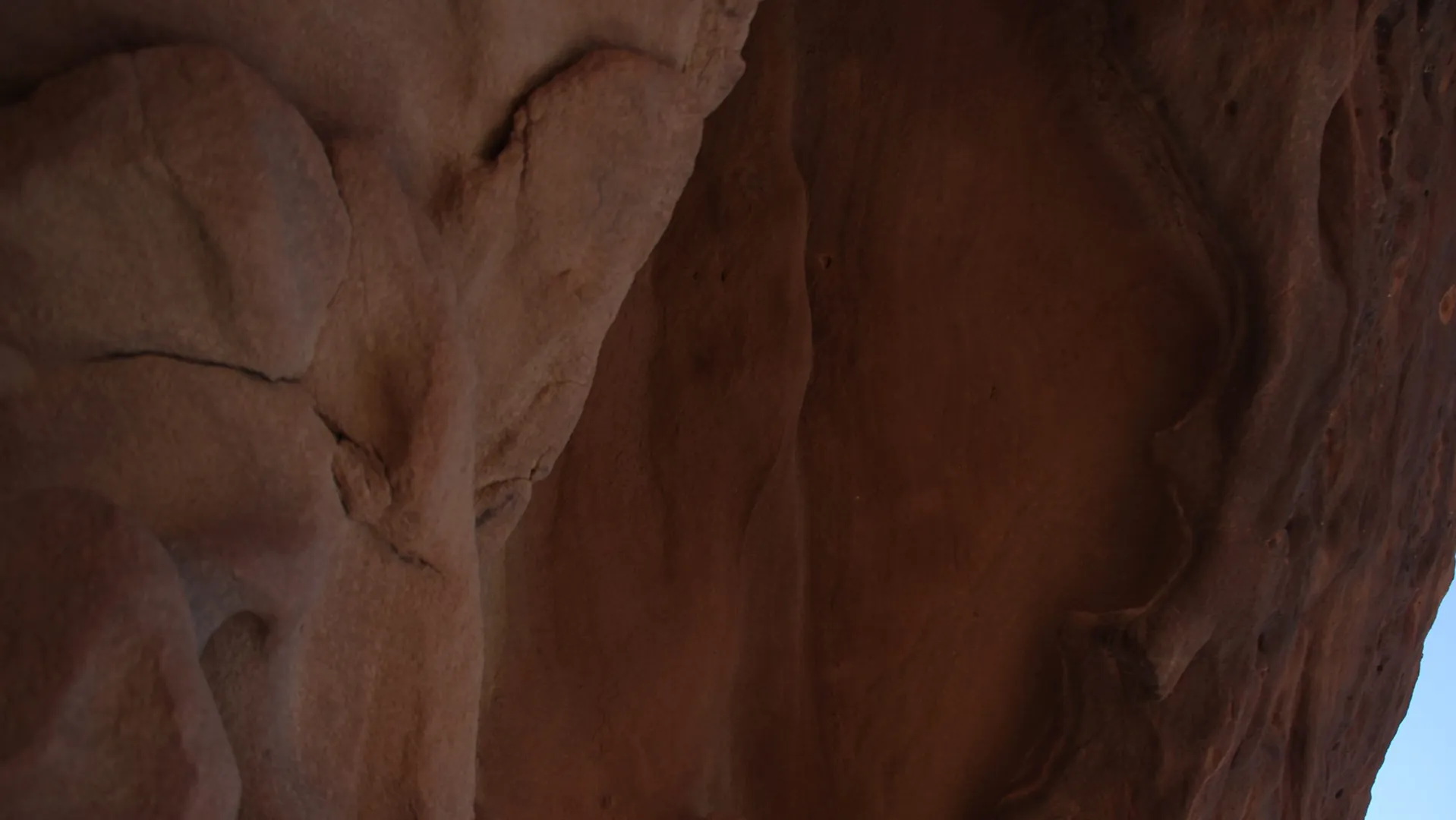 A sheer red sandstone cliff face in AlUla, with rock-cut tomb façades carved into it.