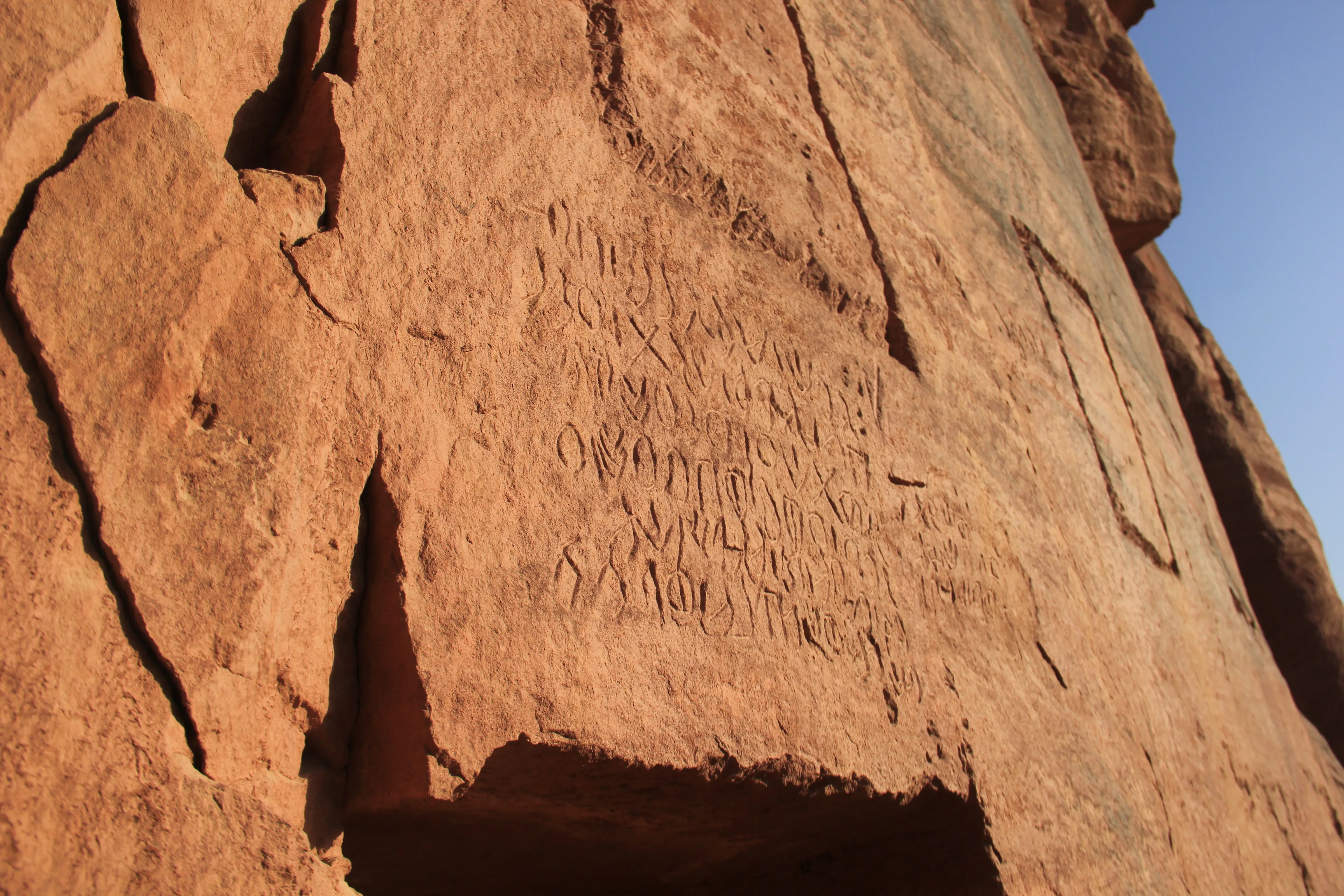 A sunlit sandstone cliff face carved with several lines of Thamudic D inscription.