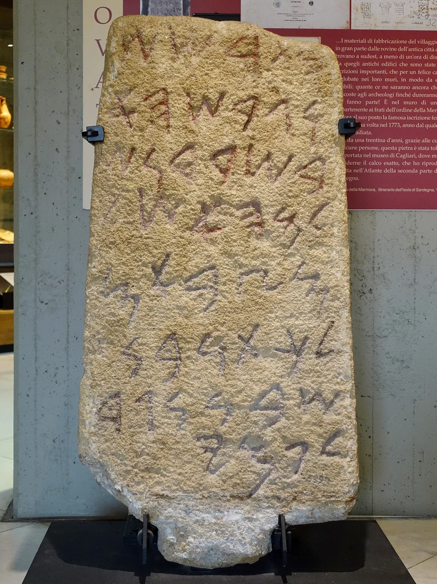 A tall sandstone stele on a museum mount, inscribed with eight lines of Old Phoenician letters.